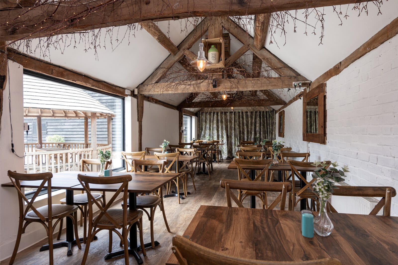 The Roost at The BarnYard, a beamed room set with wooden tables and opening onto the Courtyard