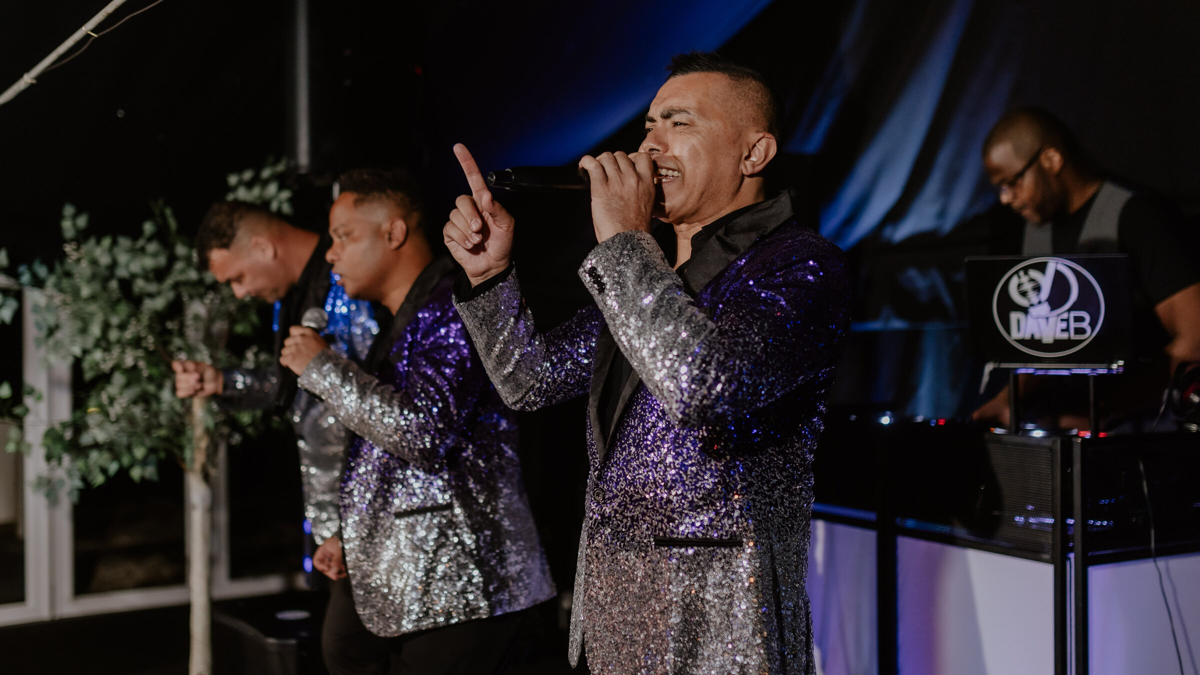 A live band in sequinned jackets performing with a DJ at an evening party at The BarnYard