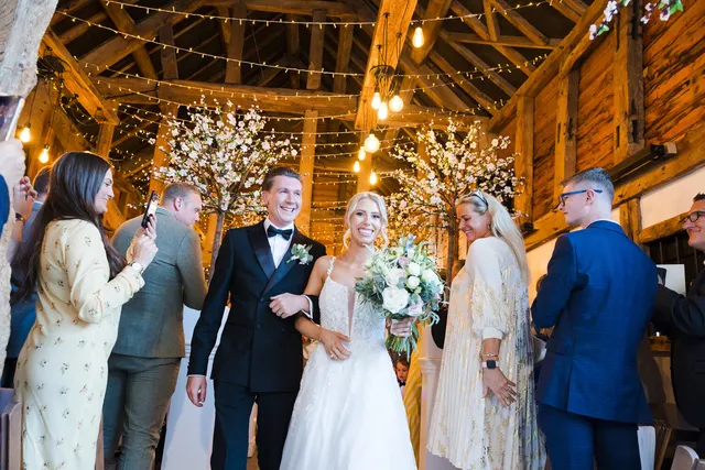 A newly married couple walk back down the aisle as guests cheer in the Apple Barn