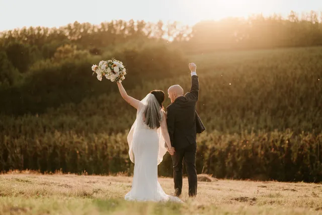 A couple raise their arms in a field at sunset