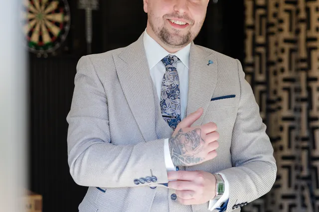 A groom in a grey three-piece suit adjusting his cuff in The Hyde Out