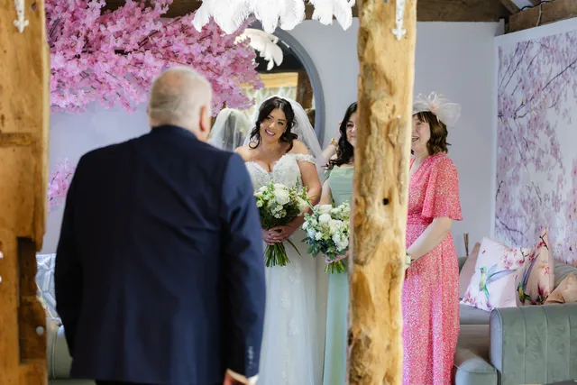 A father seeing his daughter in her dress for the first time, her mother and bridesmaid beside her