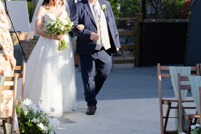 A bride walking down the outdoor aisle on her father's arm, straight from the dressing suite