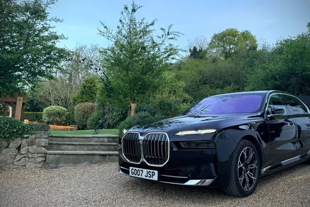 A black BMW i7 executive saloon on a gravel drive beside garden steps