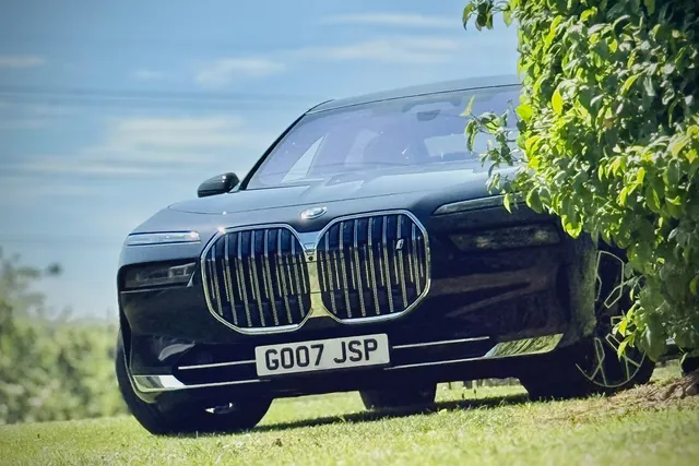 The front of a black BMW i7 parked on the grass beneath the trees