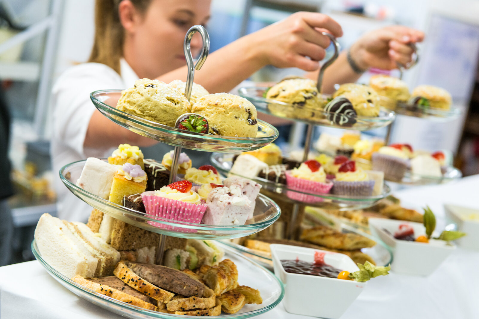 A tiered afternoon tea stand being built at The BarnYard, sandwiches, scones and cakes on glass tiers