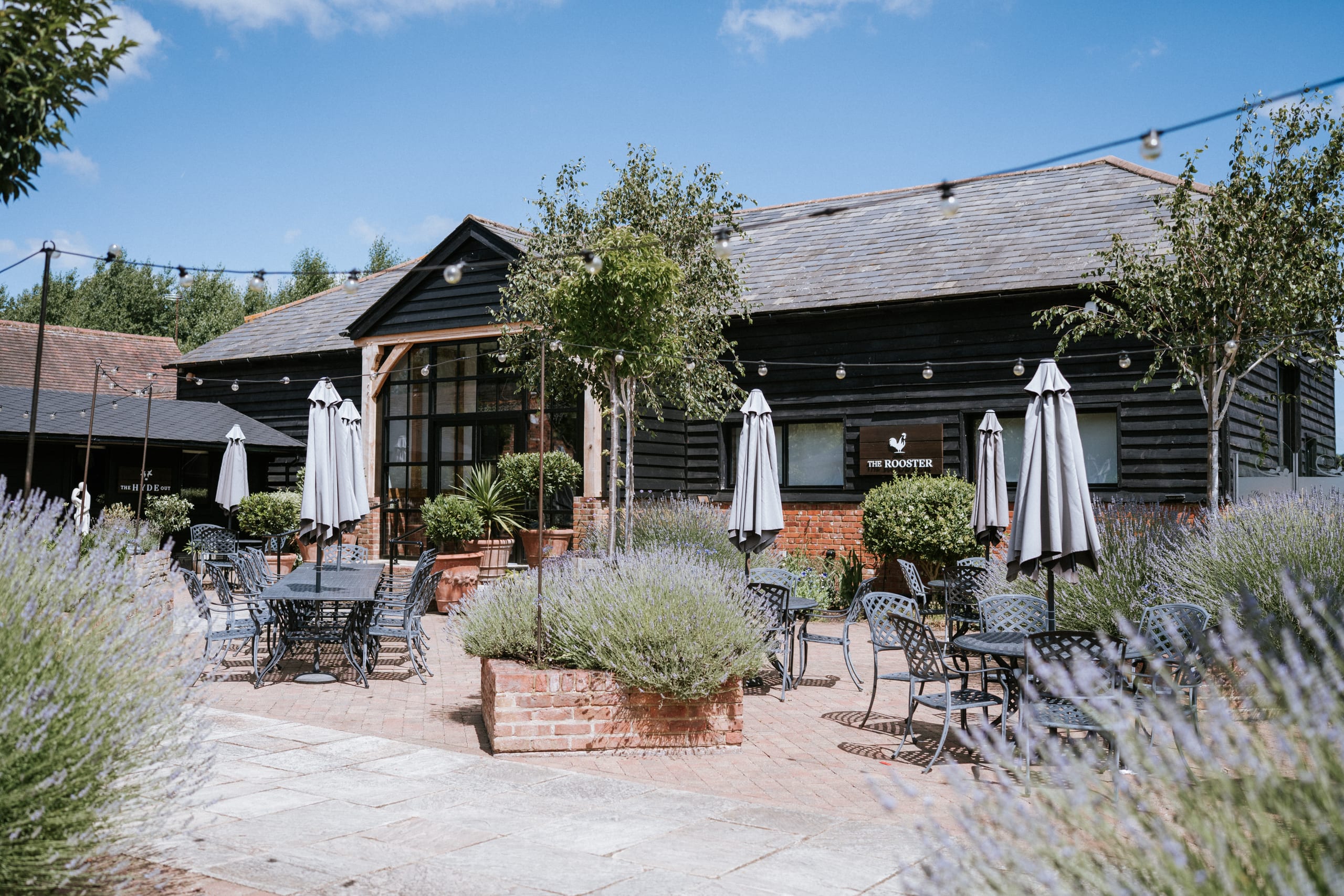 The Rooster restaurant at The BarnYard in Kent, a black timber barn with a glass A-frame entrance and terrace seating
