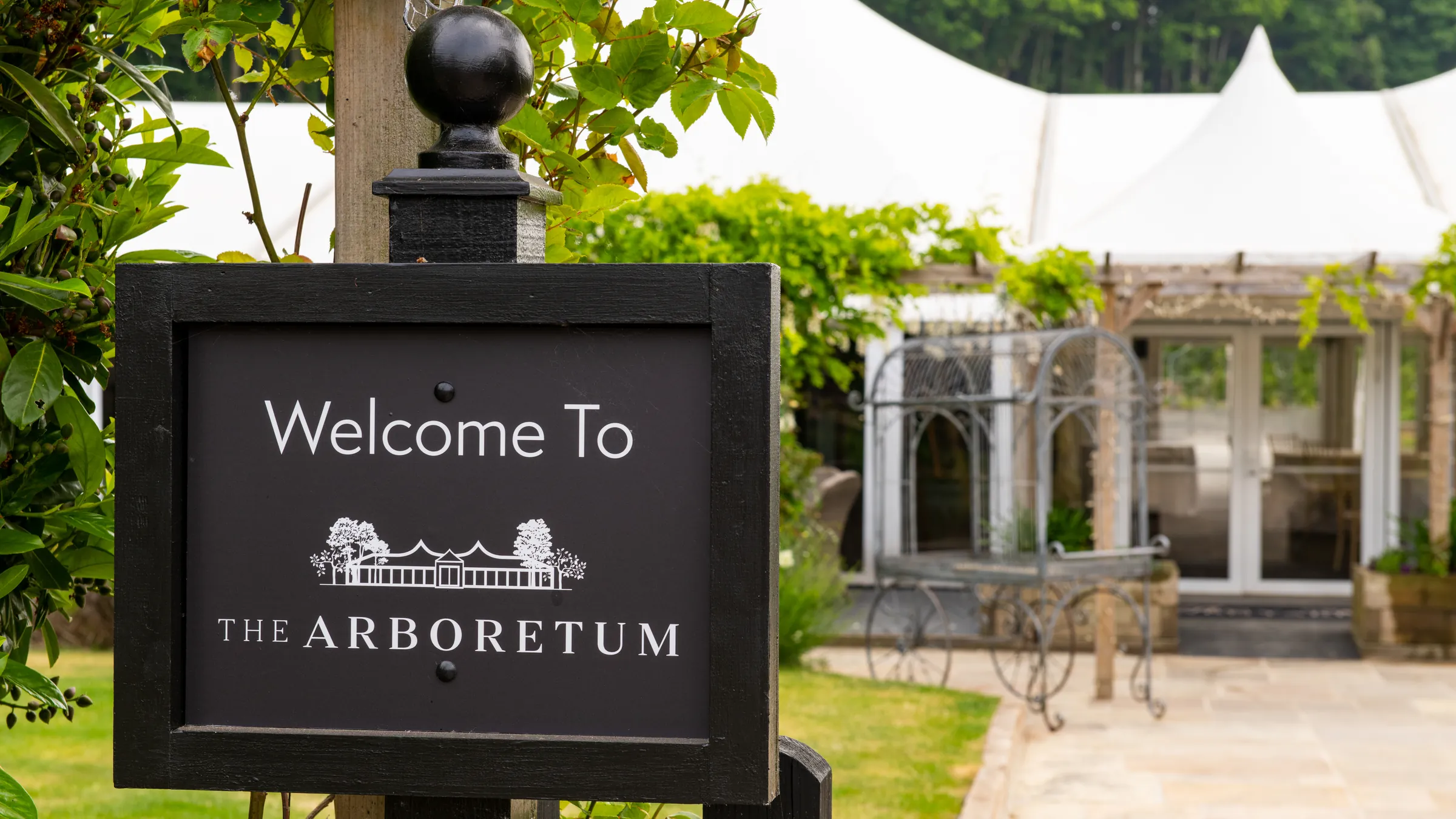 The Welcome To The Arboretum sign, with the glass pavilion behind it, at The BarnYard, Kent