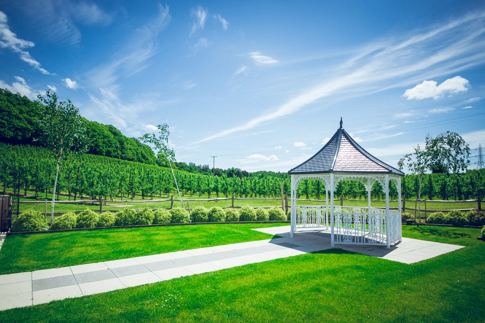 The white ceremony gazebo on the lawn at The BarnYard, with the orchards behind