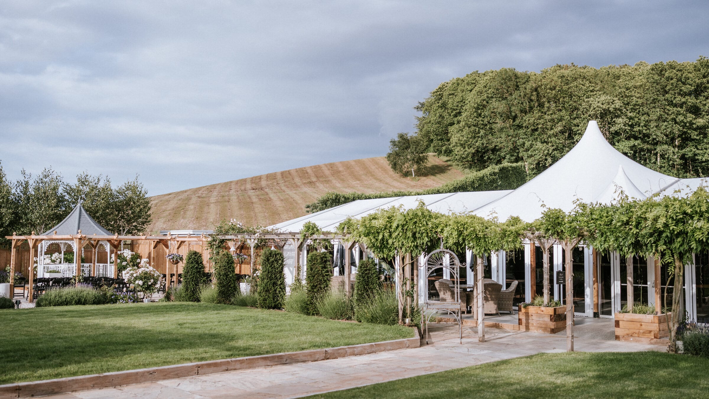 The Arboretum, The BarnYard's permanent glass pavilion, with its wisteria pergola, a ceremony gazebo and the orchard hillside behind